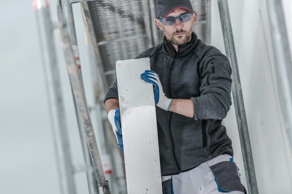 Caucasian Construction Worker Installing Insulation Material On Outside Walls Of House.